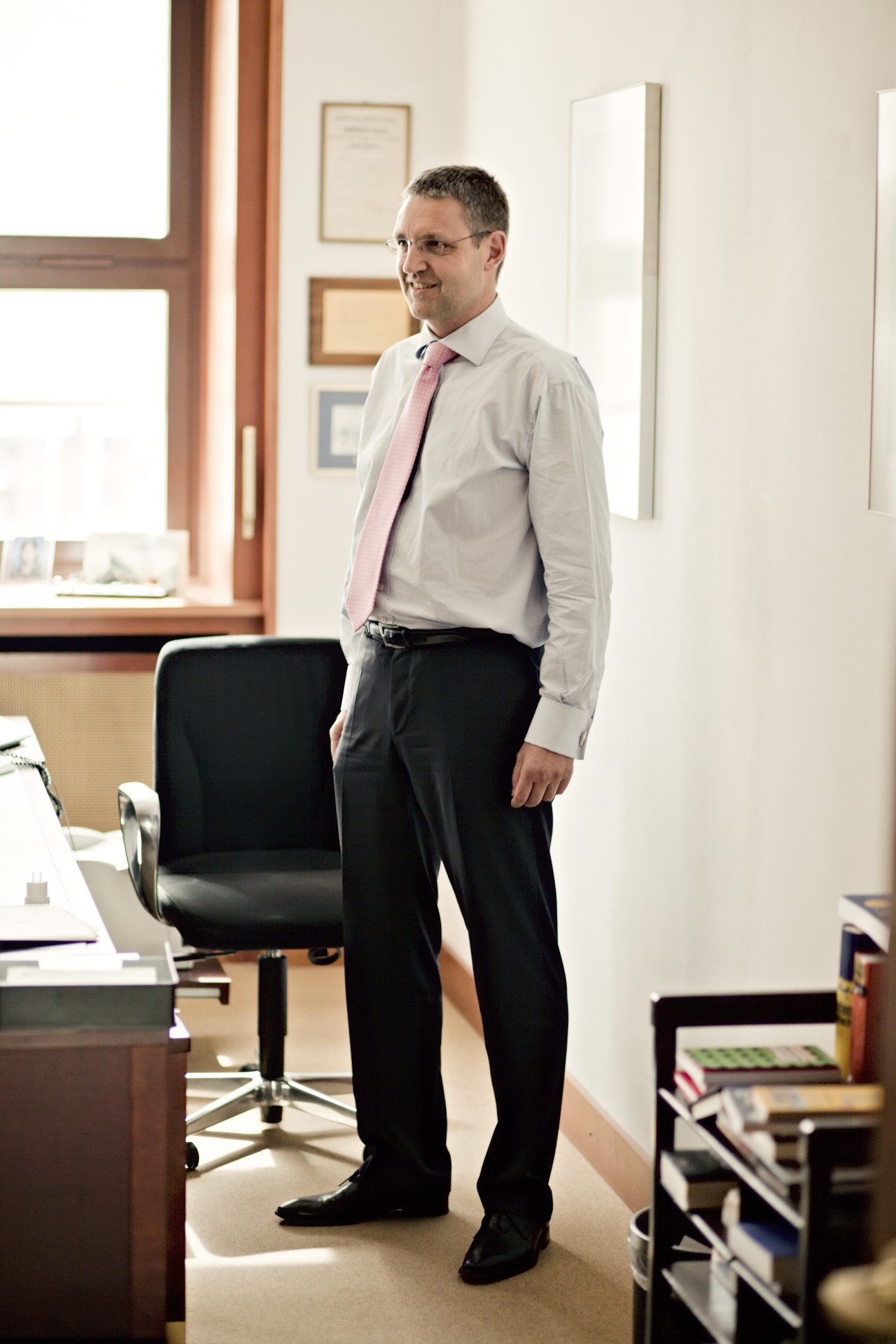 Markus Ederer stands in his office at Germany's Federal Foreign Office, wearing a light blue shirt and pink tie.