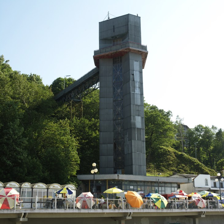 Soviet-era concrete lift tower at Svetlogorsk beach with colorful umbrellas below and green hillside behind.