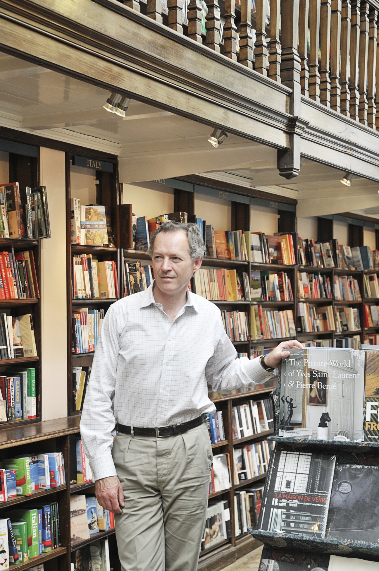 James Daunt, founder of Daunt Books, holds a book while standing in front of shelves organized by country in his Marylebone bookshop.
