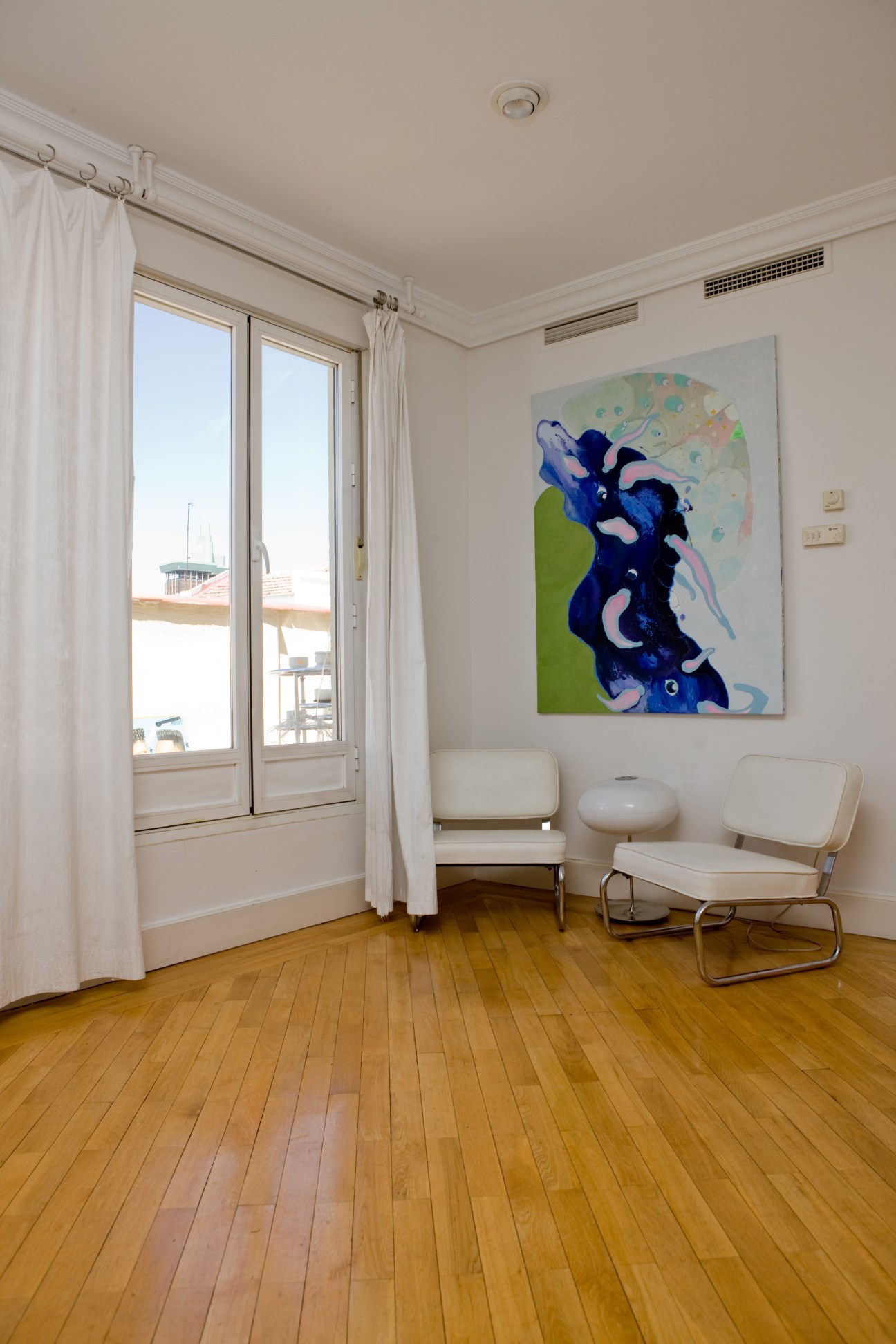 Bright attic room with wooden floors, white walls, modern artwork, and French doors opening to a terrace.