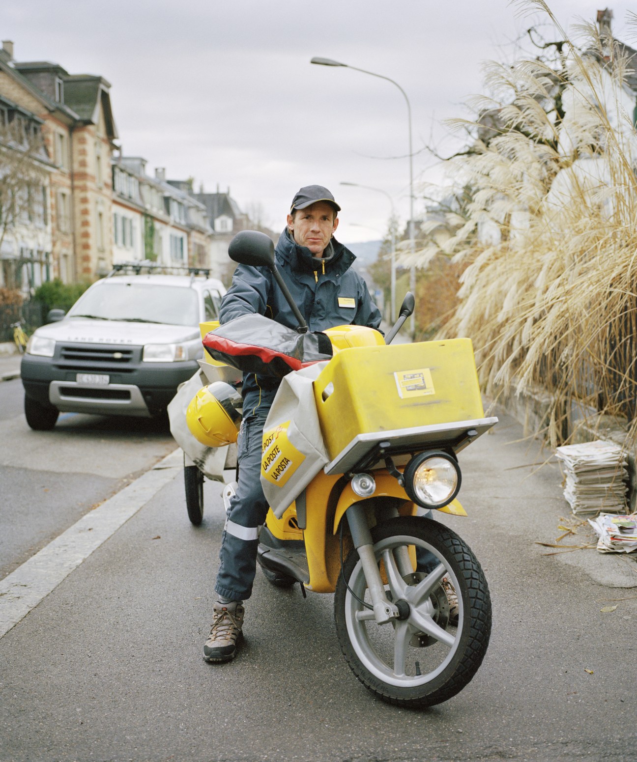 Swiss postman Herr Zeller stands with a yellow Swiss Post delivery scooter on a Bern street.