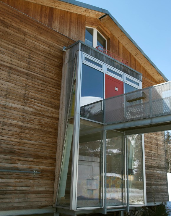 Modern wooden chalet with large windows and a metal balcony in Swiss mountains