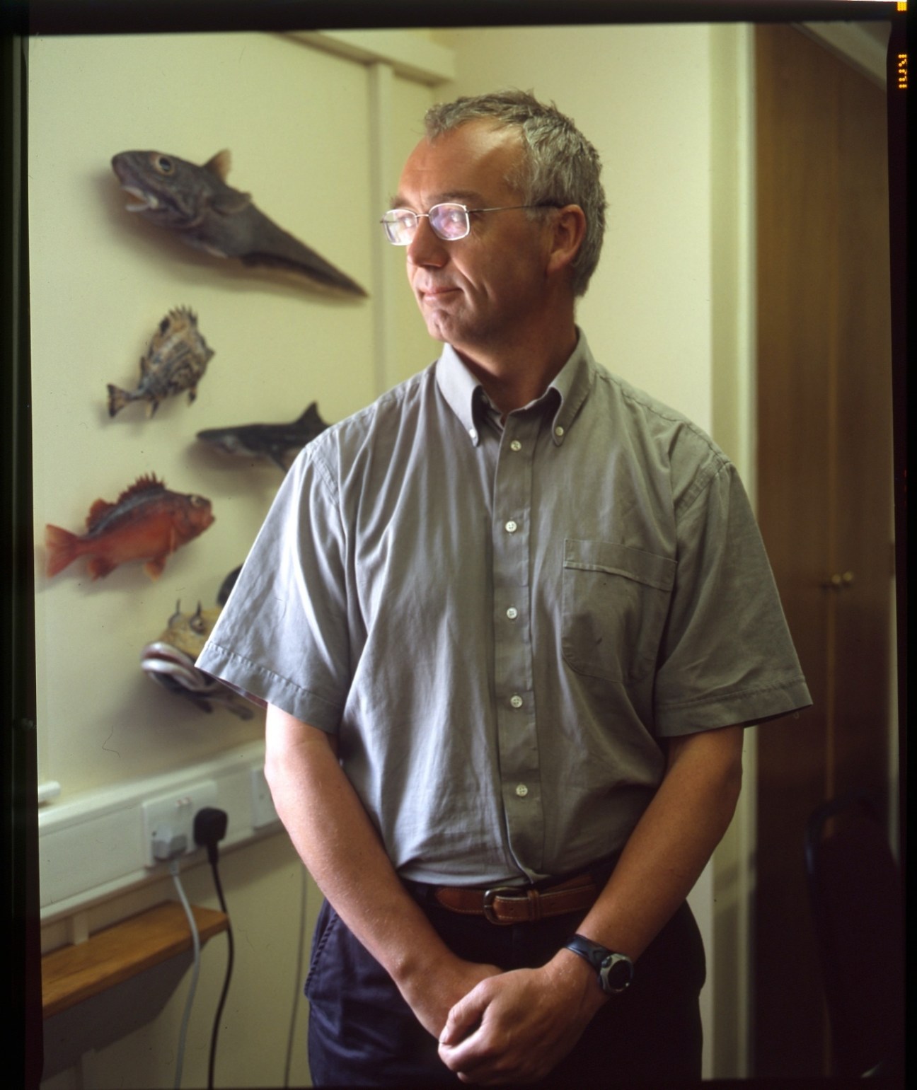 Director of Fisheries John Barton stands in front of a display of mounted fish specimens on a yellow wall.