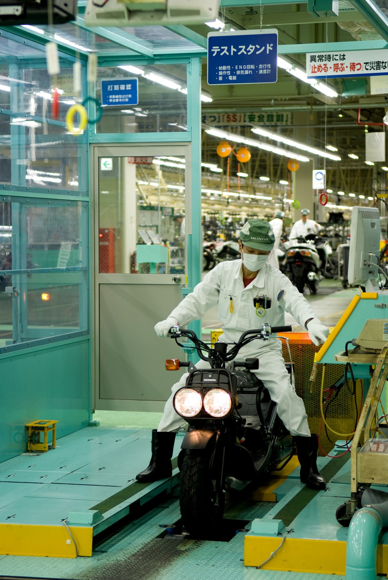 Factory worker in white protective suit tests Honda Zoomer scooter on production line.