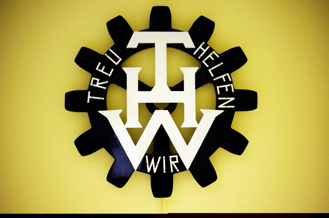 THW logo featuring a gear with white letters and text on yellow background at Berlin-Reinickendorf chapter