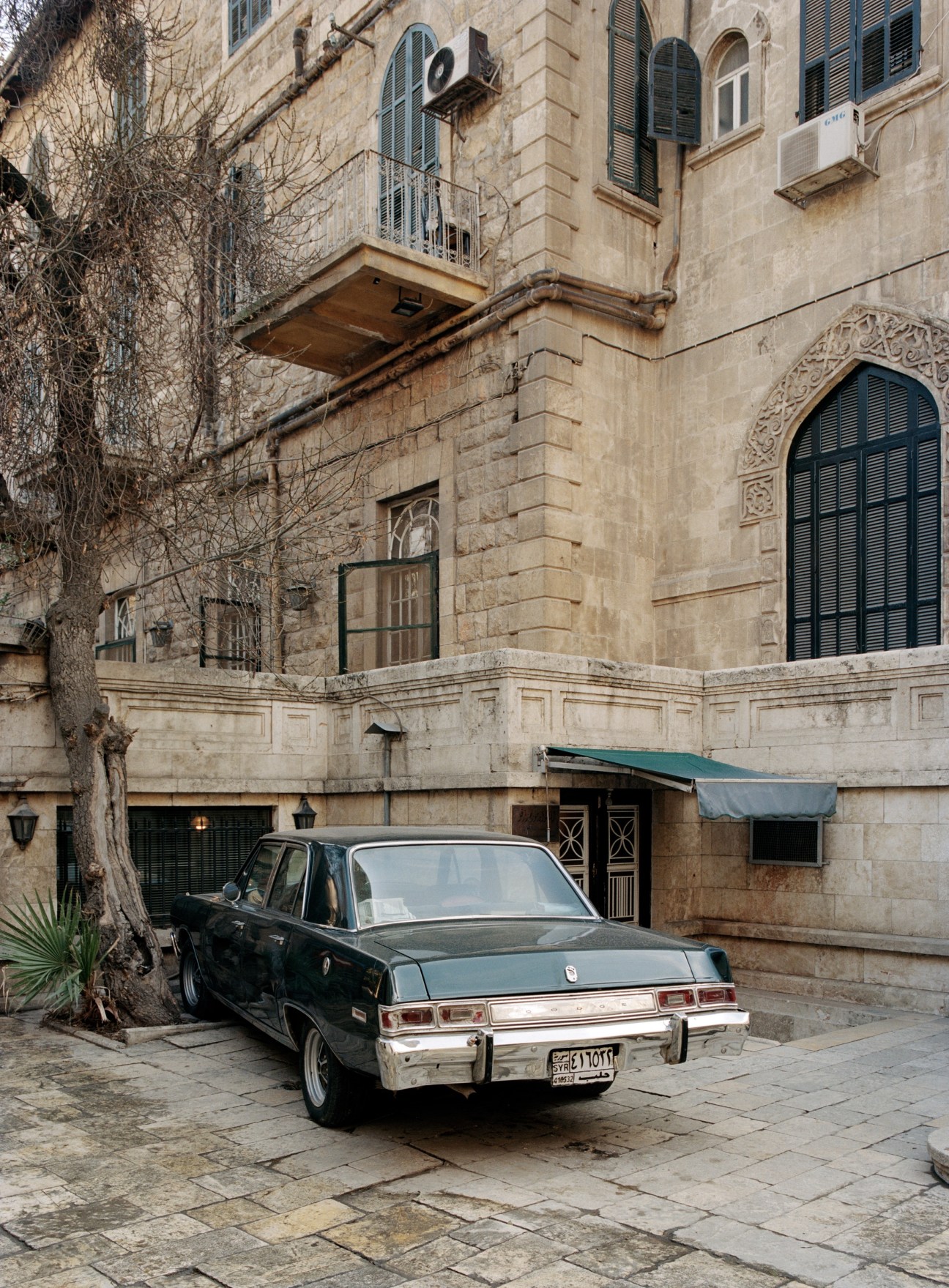 Vintage dark sedan parked in front of a historic stone building with ornate architectural details in Aleppo.