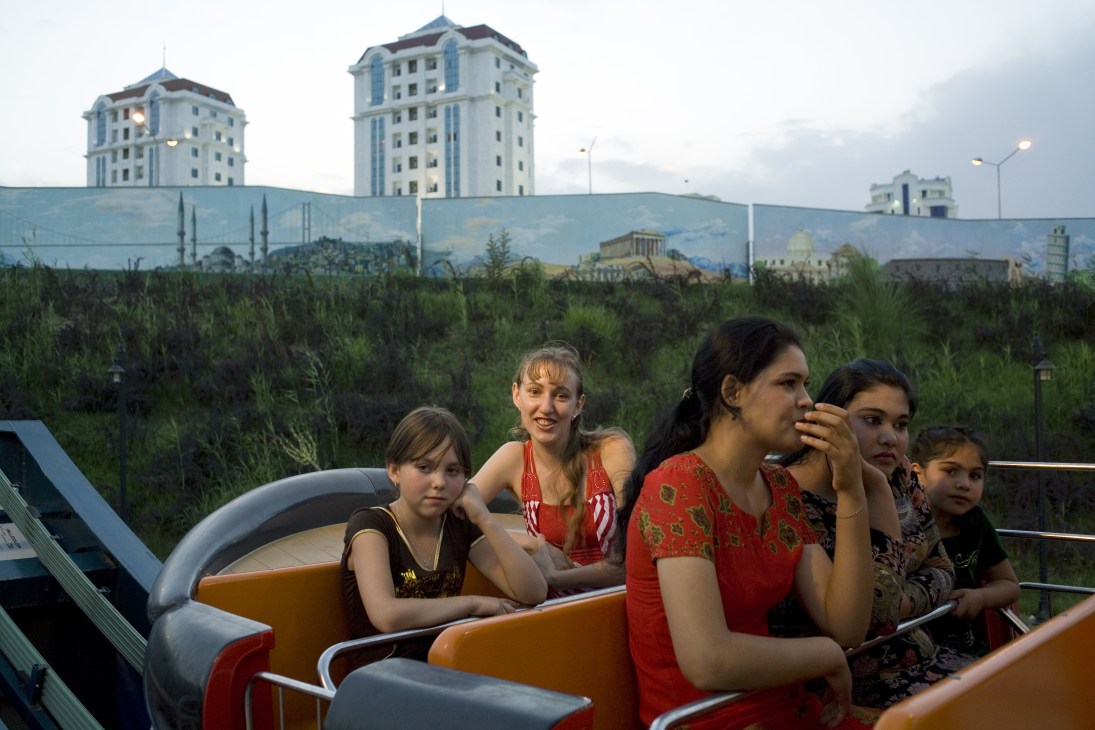 Russians and Turkmen on a ride at Ashgabat's 'World of Turkmen Fairy Tales' fairground with apartment buildings behind.