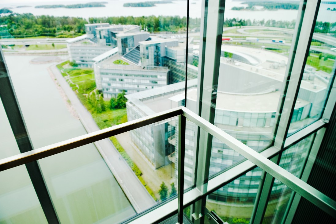 View from inside a glass elevator looking out at the Kone building in Espoo, Finland and surrounding landscape with lakes and forests.
