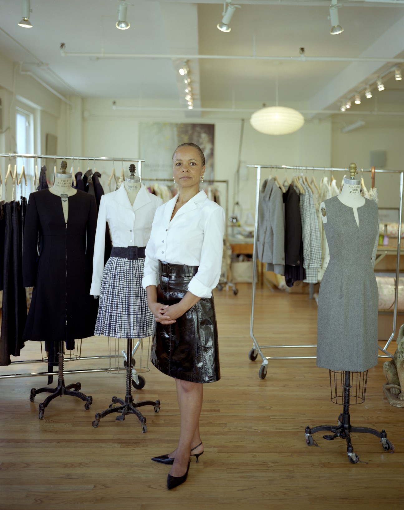 Danielle Parris stands in Melograno Editions' atelier surrounded by clothing on dress forms and racks.
