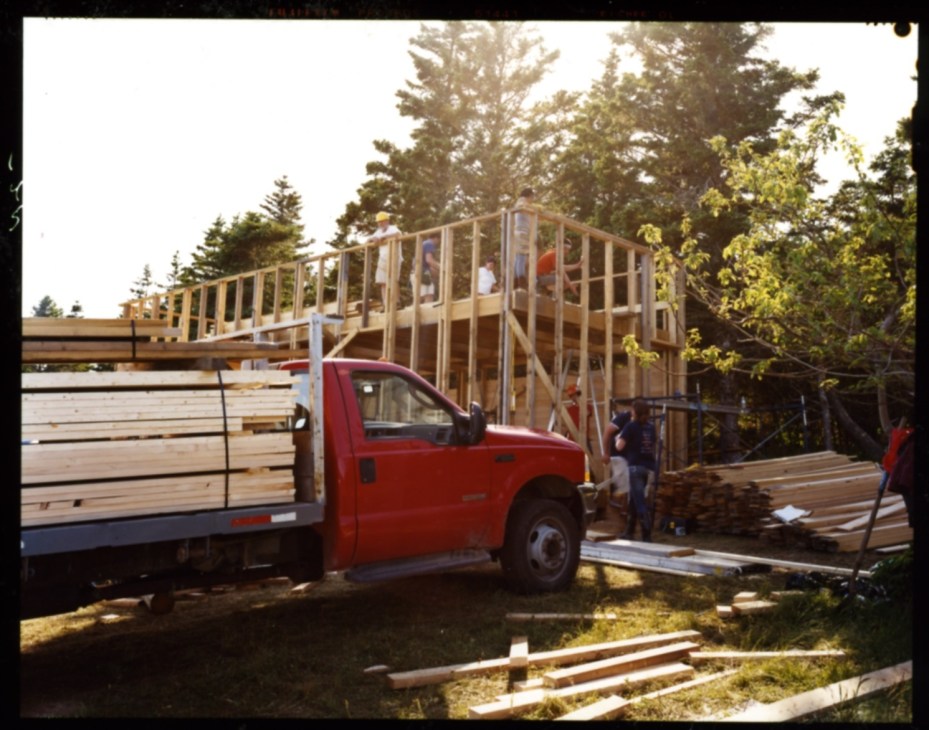 Construction site with wooden frame structure and red delivery truck with stacked lumber.