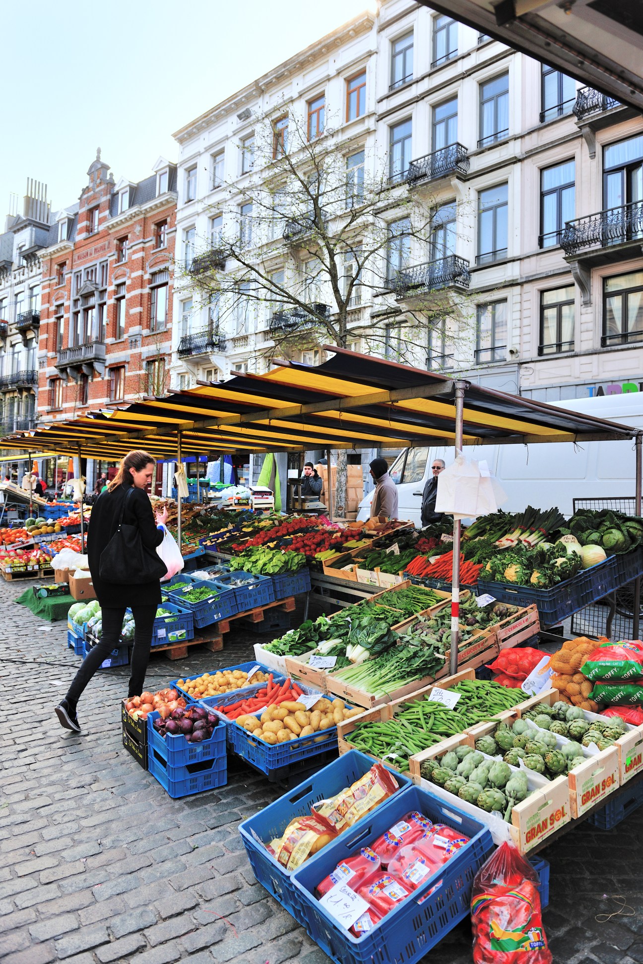 Woman shopping at Marché du Parvis de Saint-Gilles farmers market with art nouveau buildings behind.