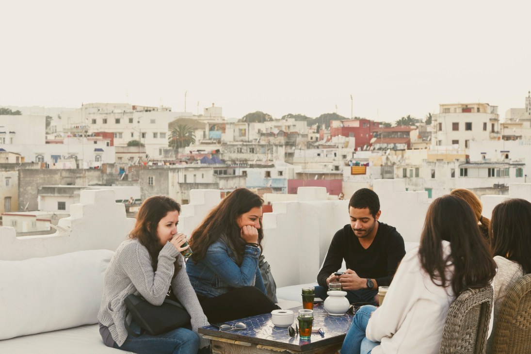 Five people enjoying tea and conversation on a white rooftop with Tangier's colorful buildings in the background.