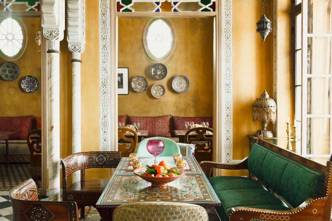 Ornate dining room with golden yellow walls, intricate carved white columns, decorative plates, and traditional Moroccan furniture.