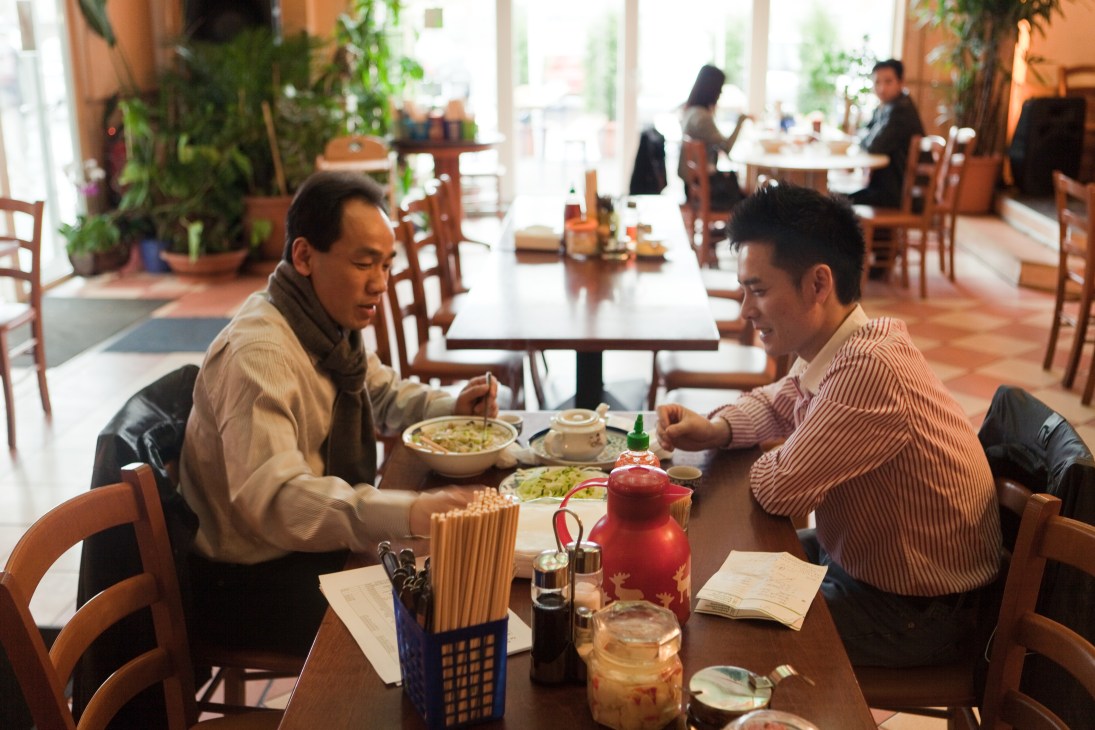 Two Vietnamese men having lunch at a restaurant table at Dong Xuan Center in Berlin.