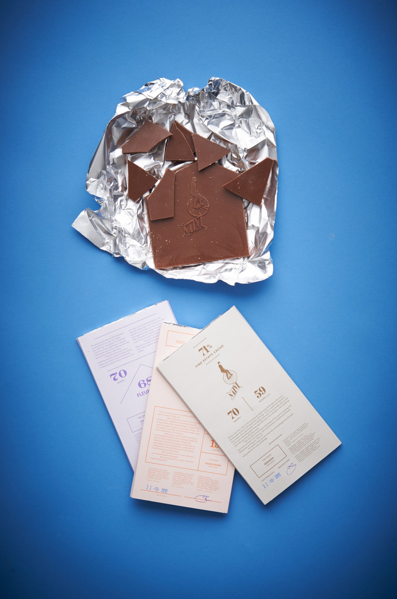 Chocolate Naive bar unwrapped with packaging and printed materials on blue background