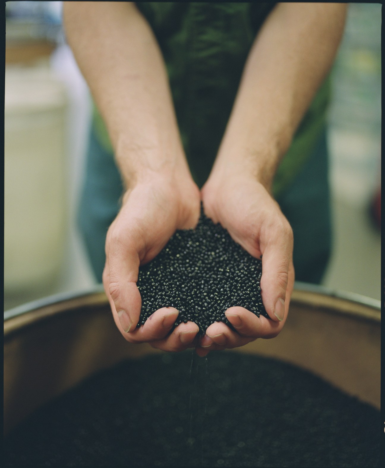 Hands holding black plastic pellets used in Pelican case manufacturing.