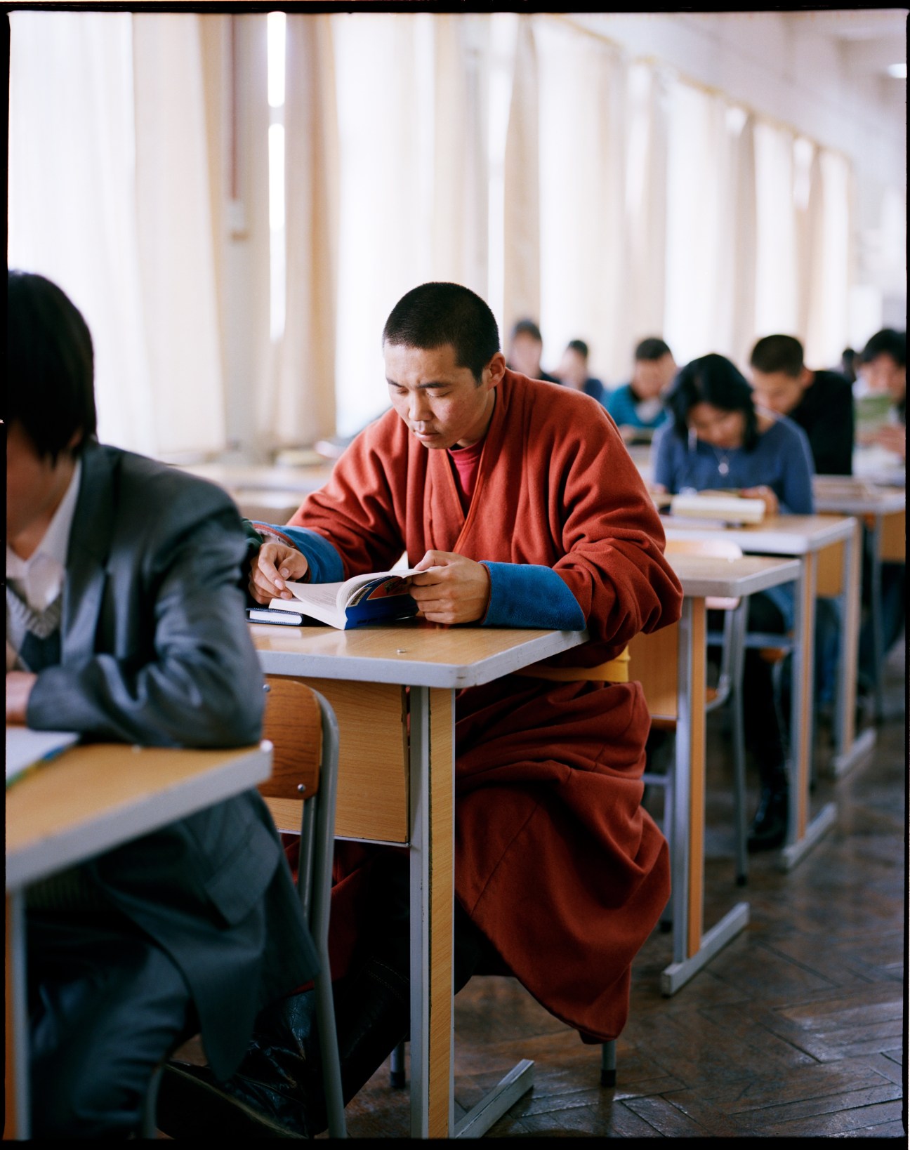 Monk in red and blue robes reading at a desk in Ulan Bator's central library.
