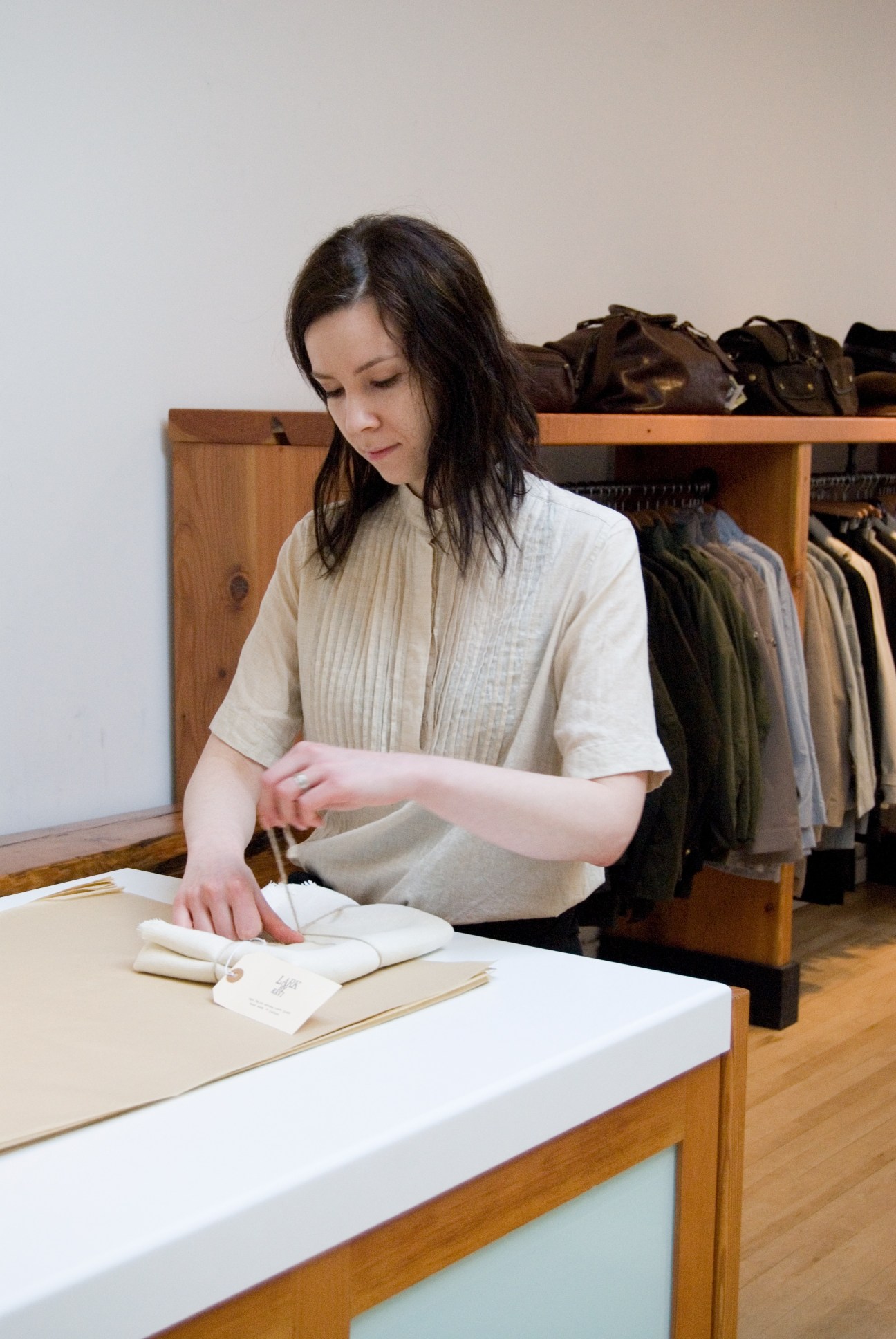 Veronika Baspaly, co-owner of Lark, examining fabric swatches at a wooden counter with clothing hanging on a rack behind her.