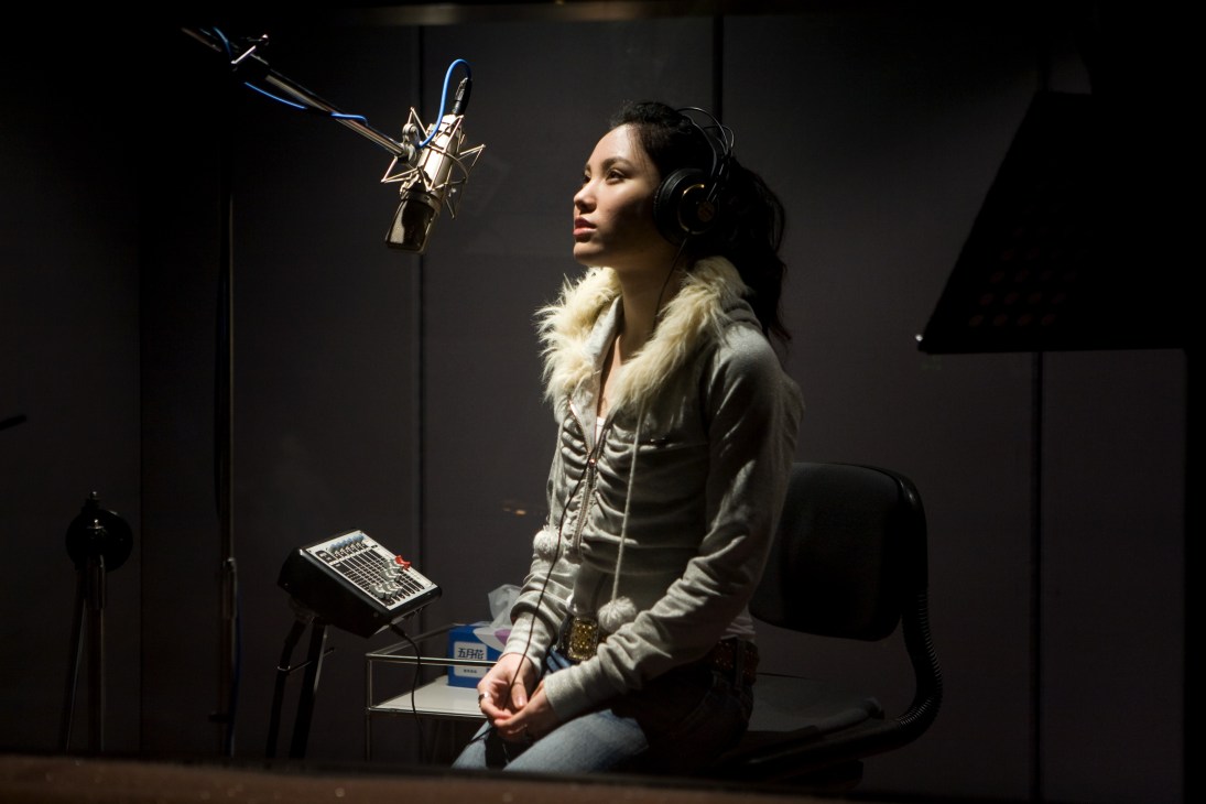 Female singer Alisa recording in a studio, wearing headphones and a white quilted jacket.