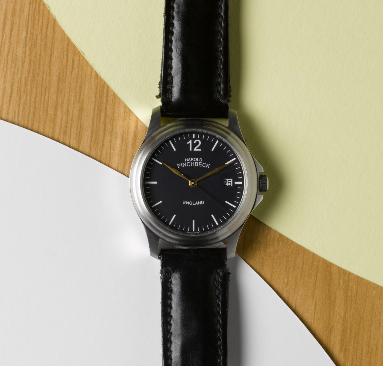 Harold Pinchbeck watch with black dial and leather strap on geometric background