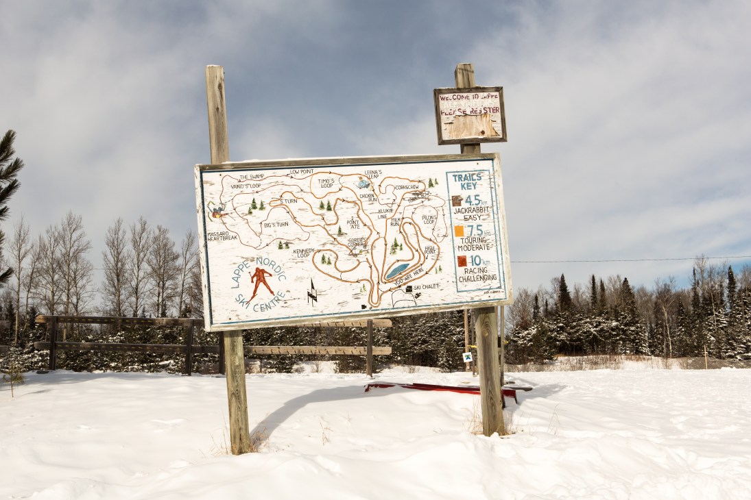 Wooden trail map sign for Lappe Nordic Ski Club with ski routes marked in snowy landscape.