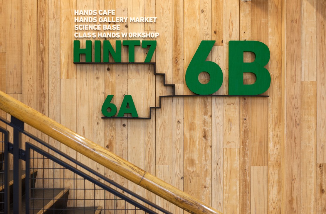 Green floor level signage for HINT7 6B and 6A on wooden wall with staircase railing.