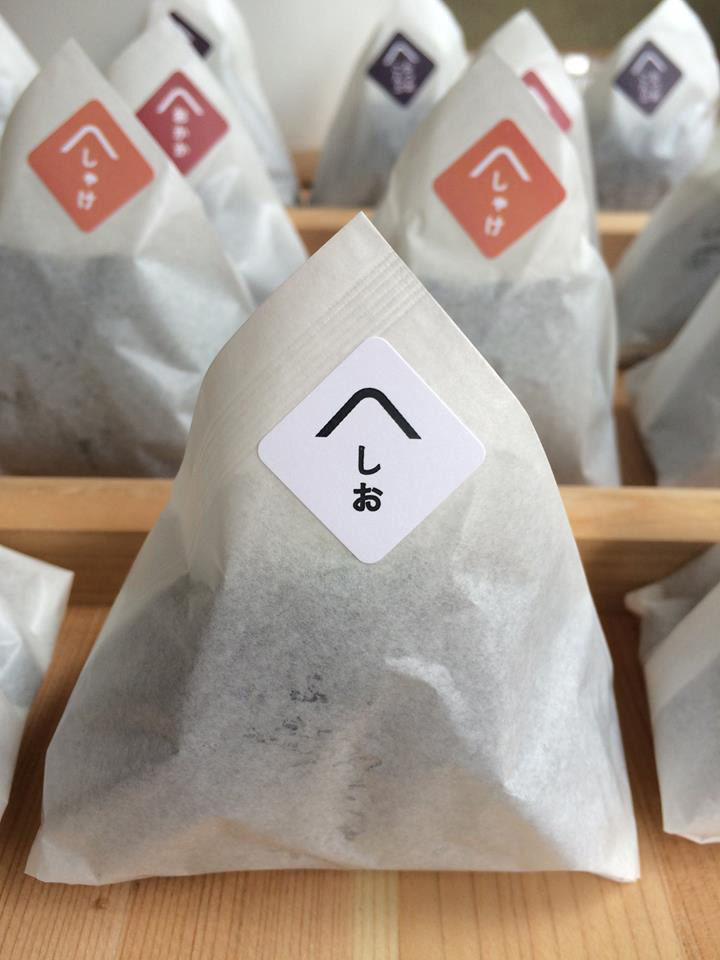 Packaged onigiri rice balls with Japanese labels displayed on wooden shelf at Okomeya Tokyo.