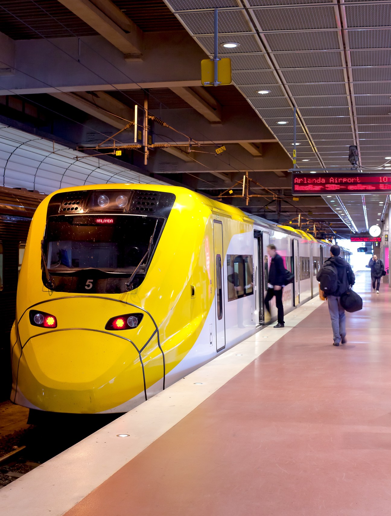 Yellow and white Arlanda Express train at Stockholm airport station platform with passengers boarding.