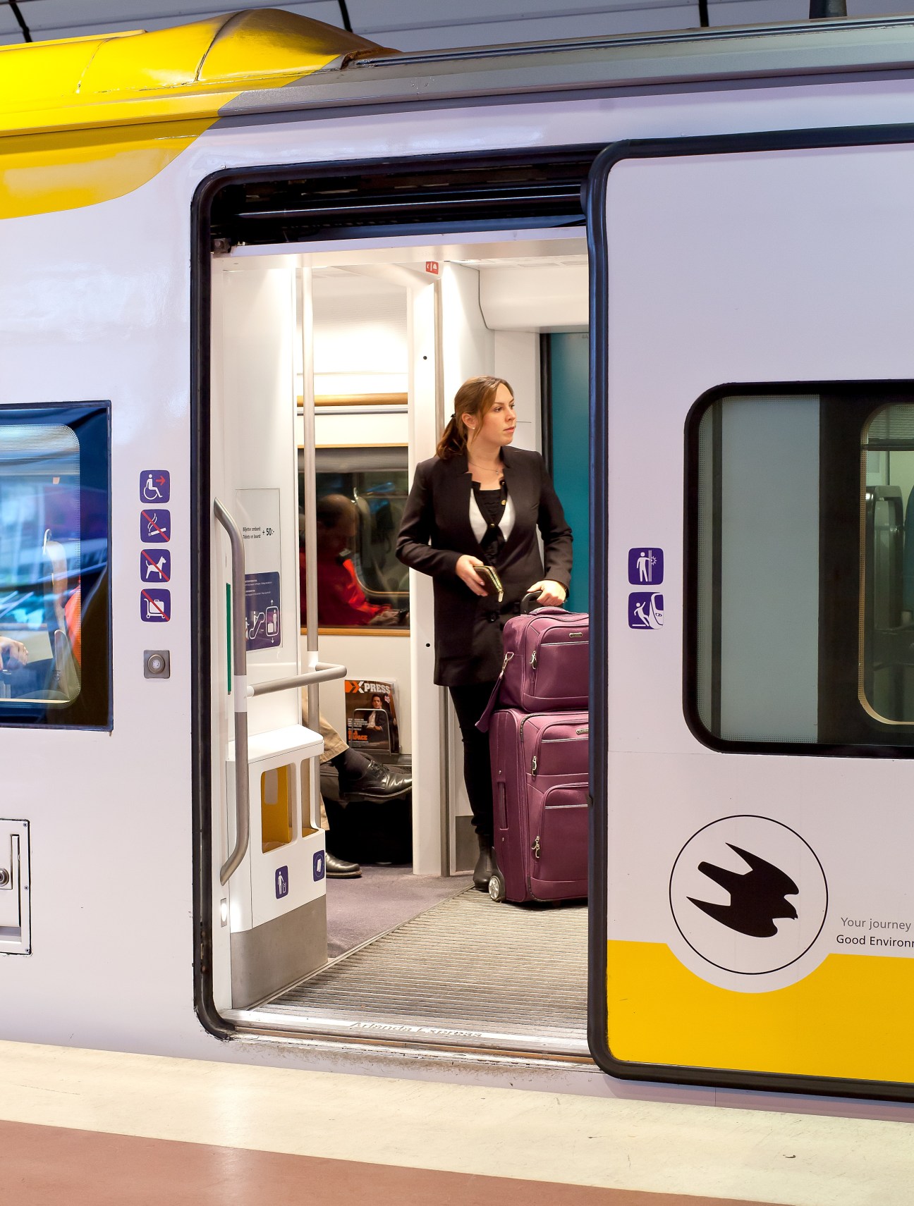 Woman standing in doorway of Arlanda Express train with purple luggage visible inside.