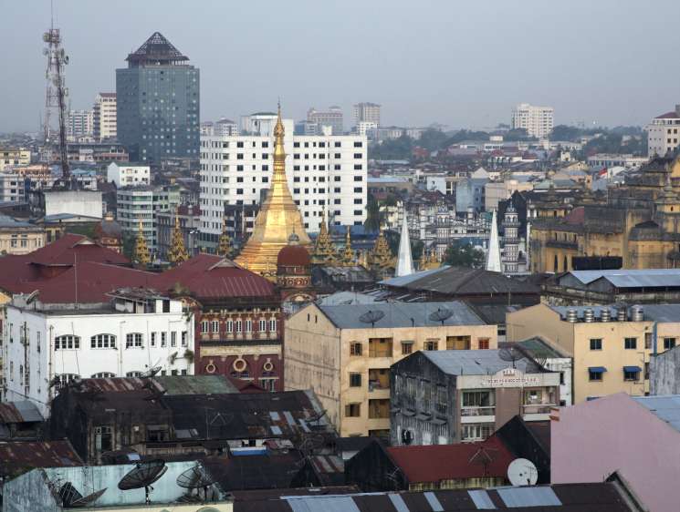 Yangon skyline showing colonial and modern architecture with golden pagoda at center.