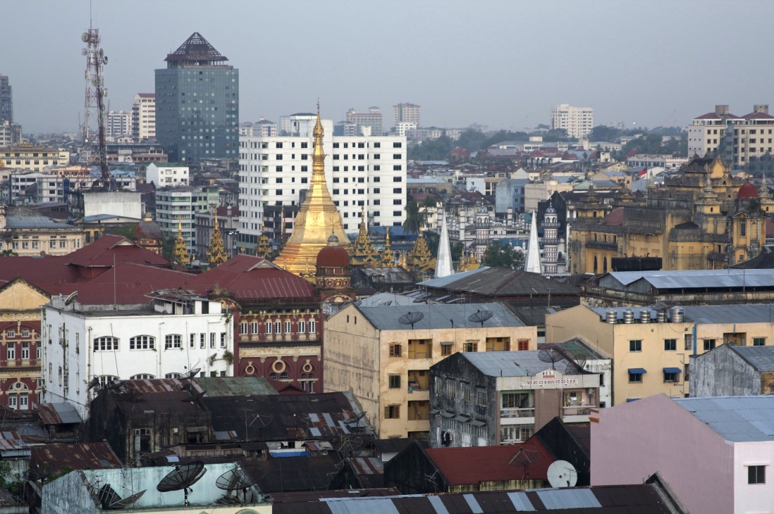Yangon skyline showing colonial and modern architecture with golden pagoda at center.