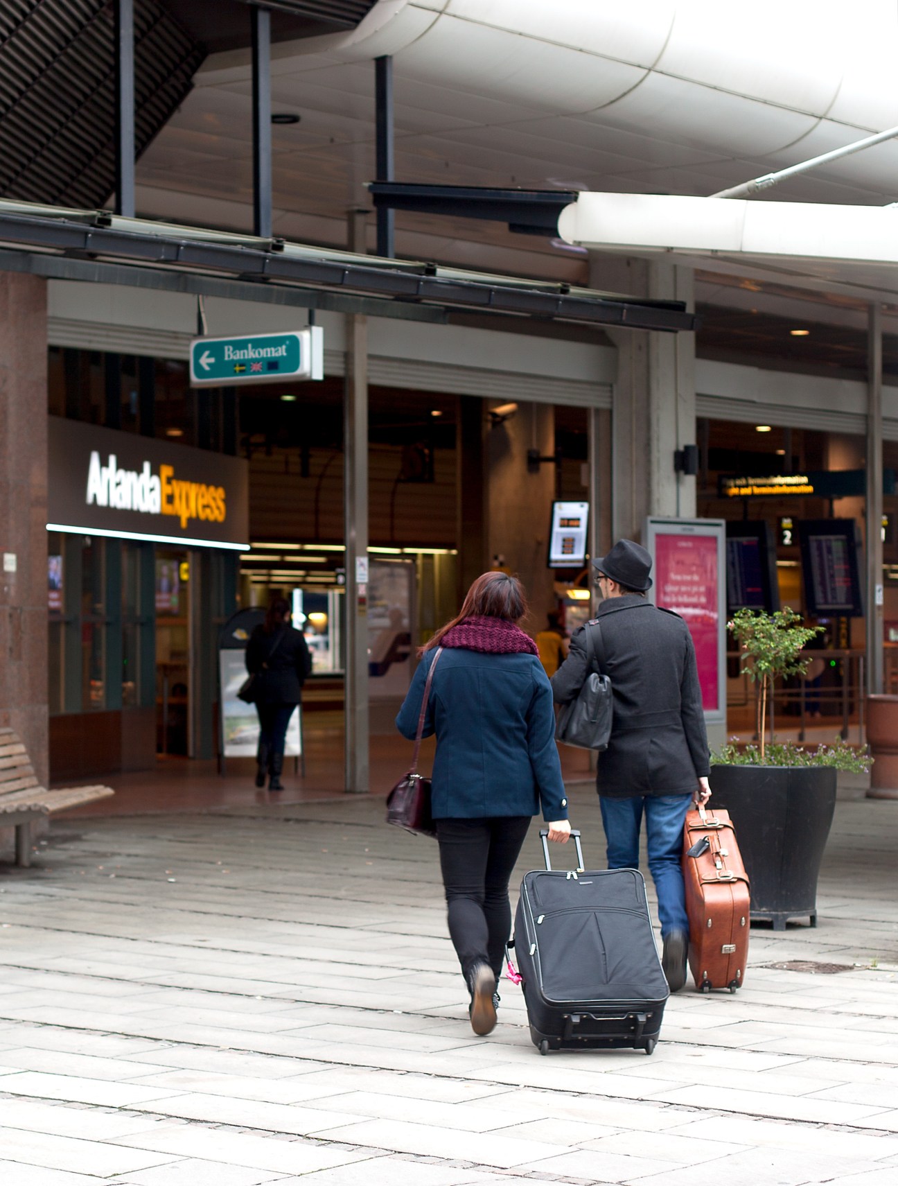 Two travelers with rolling luggage walking through a modern airport terminal corridor.