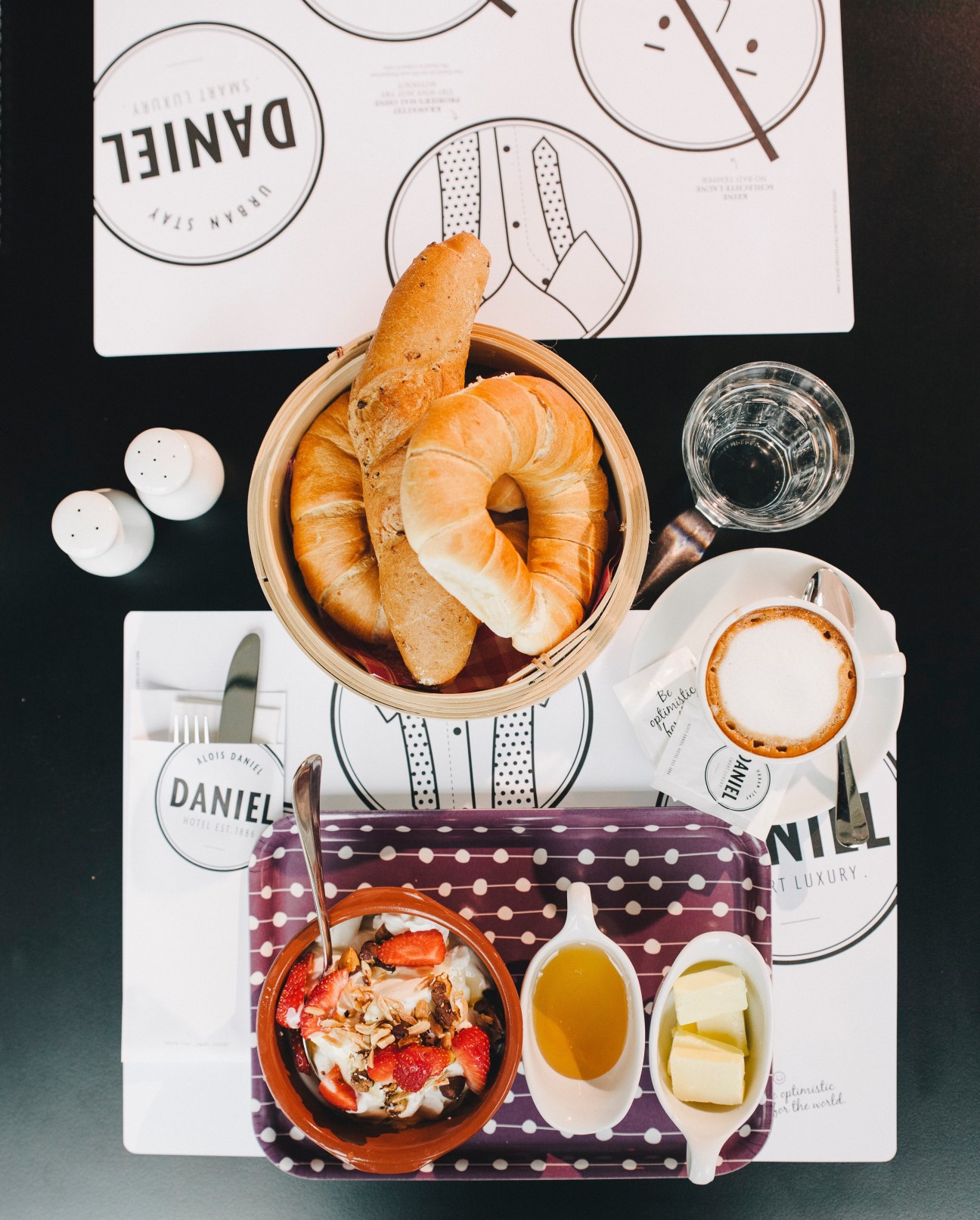 Hotel Daniel Vienna breakfast spread with pastries, coffee, and branded tableware on dark table.