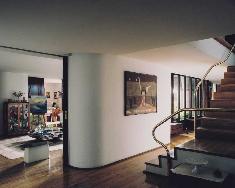 Modernist apartment interior with curved walls, spiral staircase with brass railing, artwork, and wooden flooring in Torres Blancas.