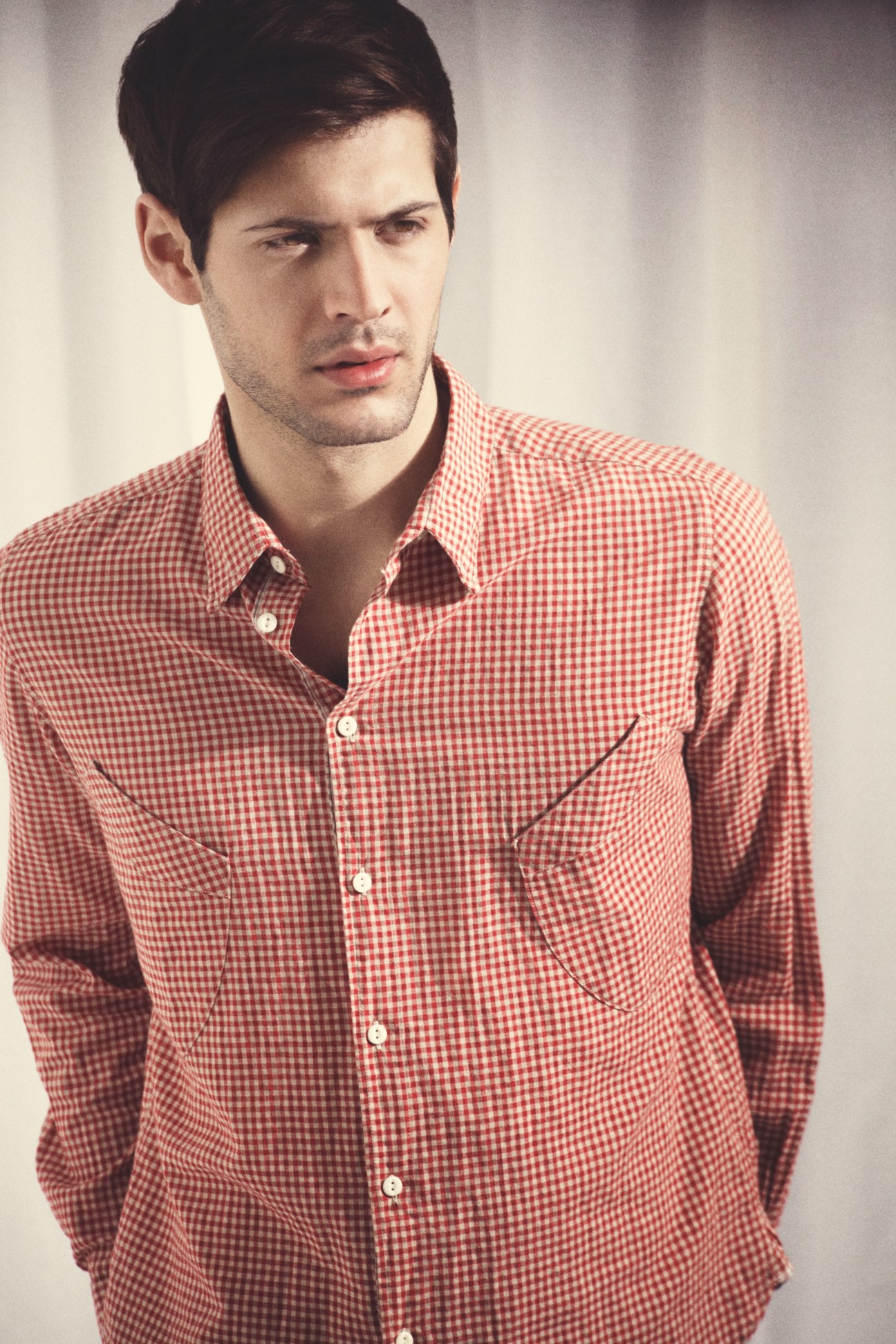 Man wearing a red and white gingham button-up shirt with chest pocket detail.