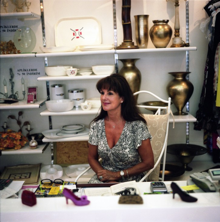 Valerie Segal seated at a desk in front of shelving displaying decorative ceramics and brass vessels.
