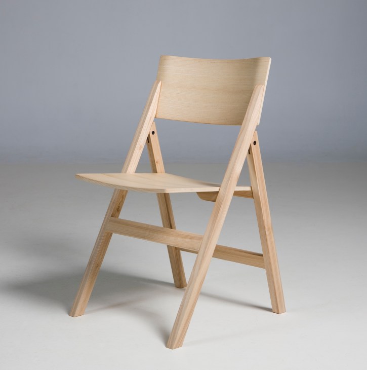 Light wooden folding chair with angled legs and curved backrest against gray background.