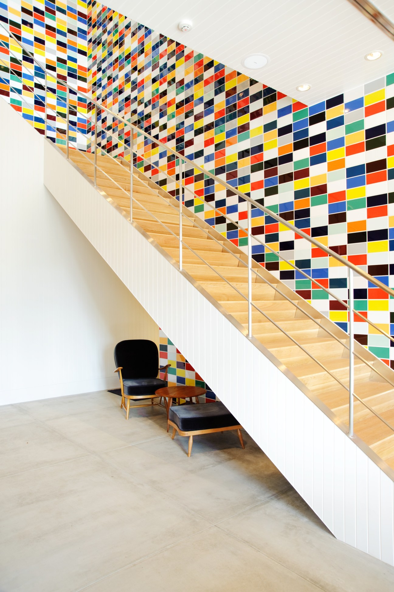 Colorful stairwell with multicolored tile wall installation and wooden stairs at the Soho office building.