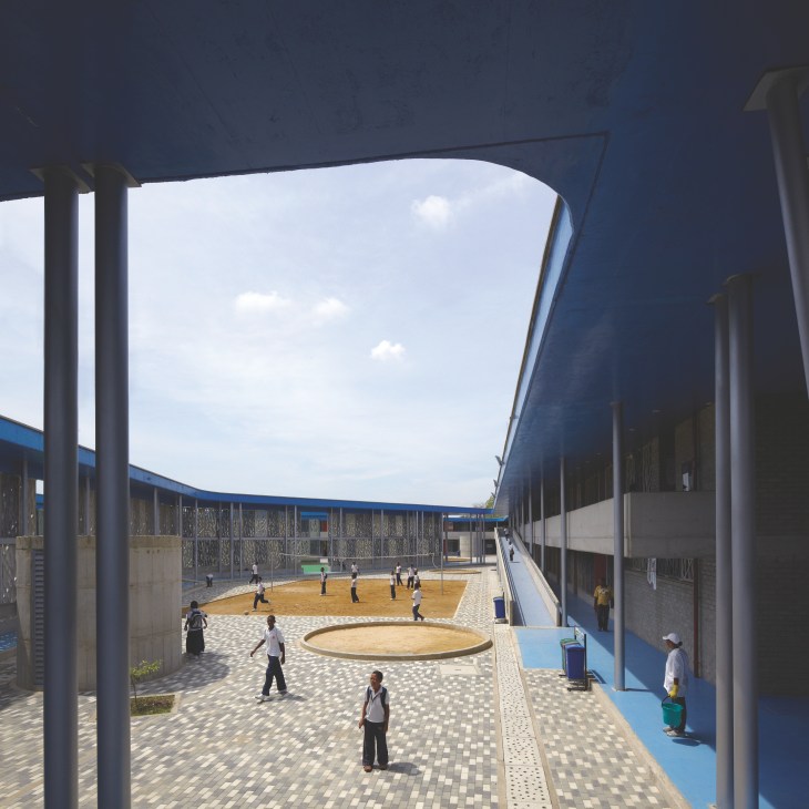 Students play in a covered outdoor courtyard of Flor del Campo school with concrete fretwork providing shade.