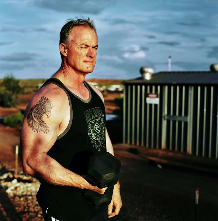 Kim Whittaker, crane operator for Consolidated Miners, holding a dumbbell at a mining camp in Western Australia's Pilbara region.