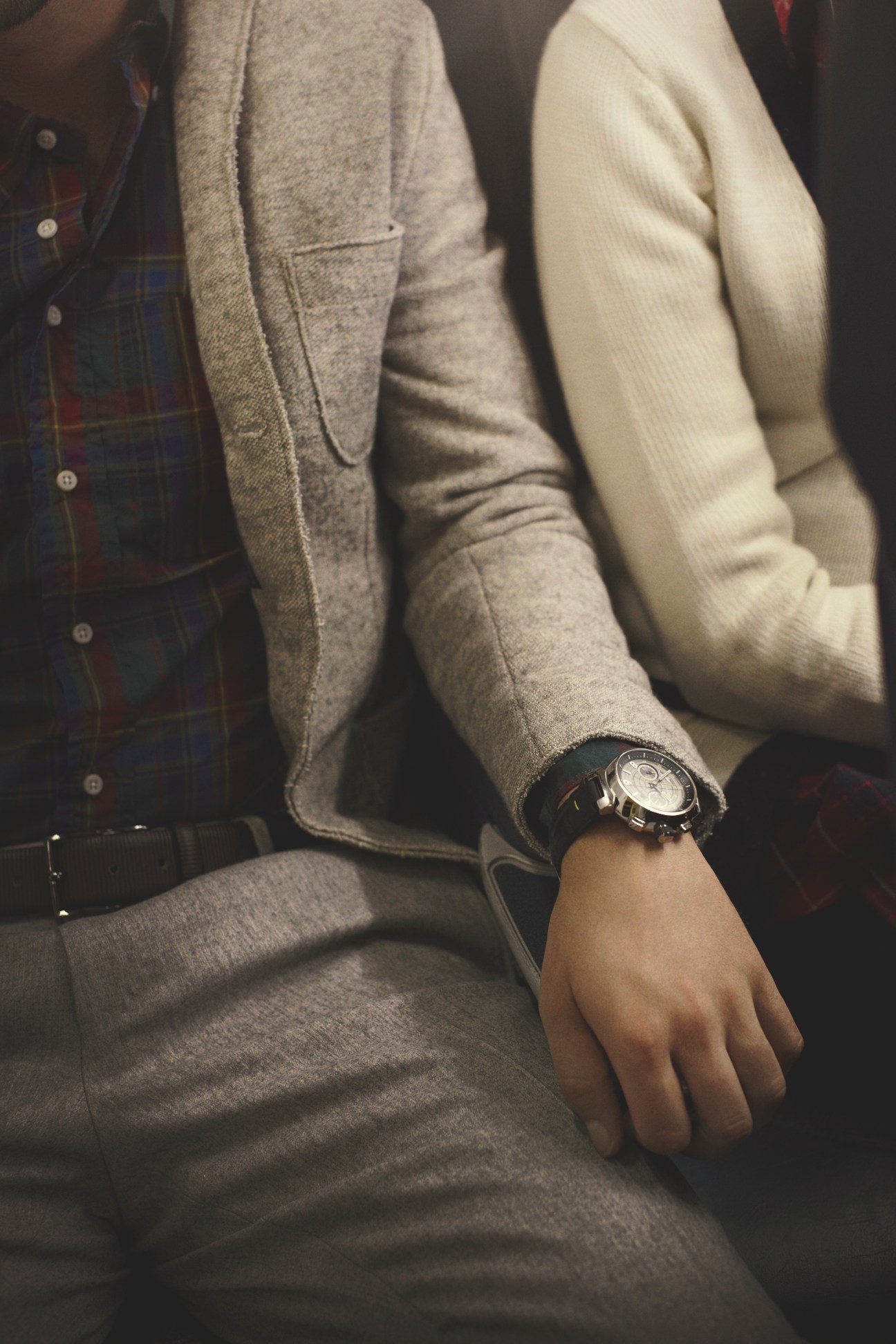 Three people seated closely, wearing tailored jackets and sweaters, with focus on a Louis Vuitton watch.