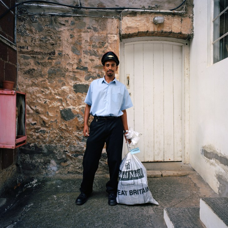 Royal Mail postal worker in uniform delivering mail bag on St Helena island street.