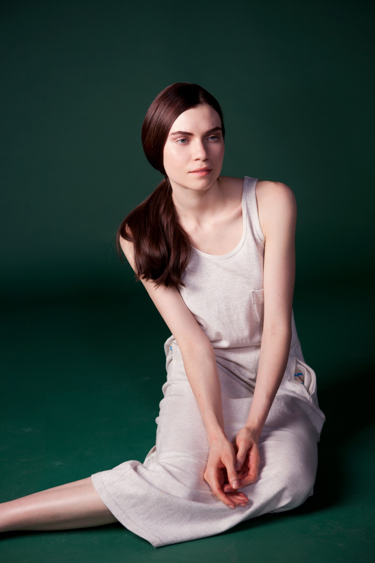 Woman wearing soft grey sleeveless tank top and light grey skirt against green background.