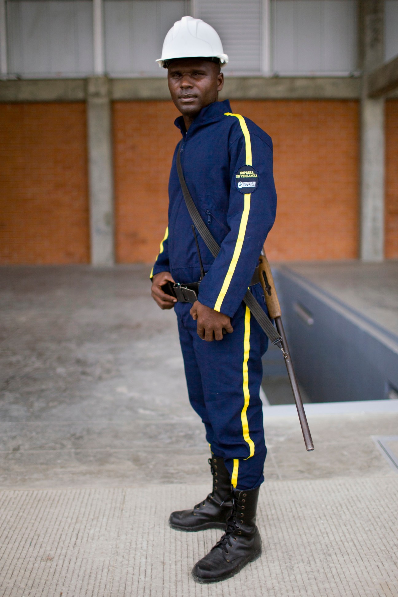 Port security guard in Buenaventura wearing white hard hat, blue uniform with yellow stripe, and carrying rifle.