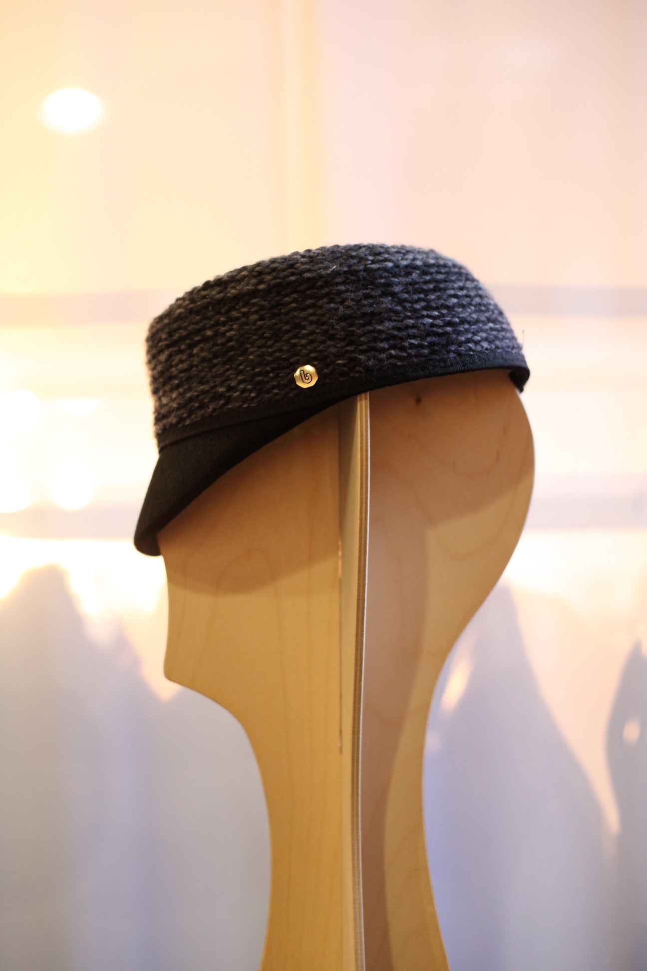 Black knitted wool hat with gold button detail displayed on wooden mannequin head.
