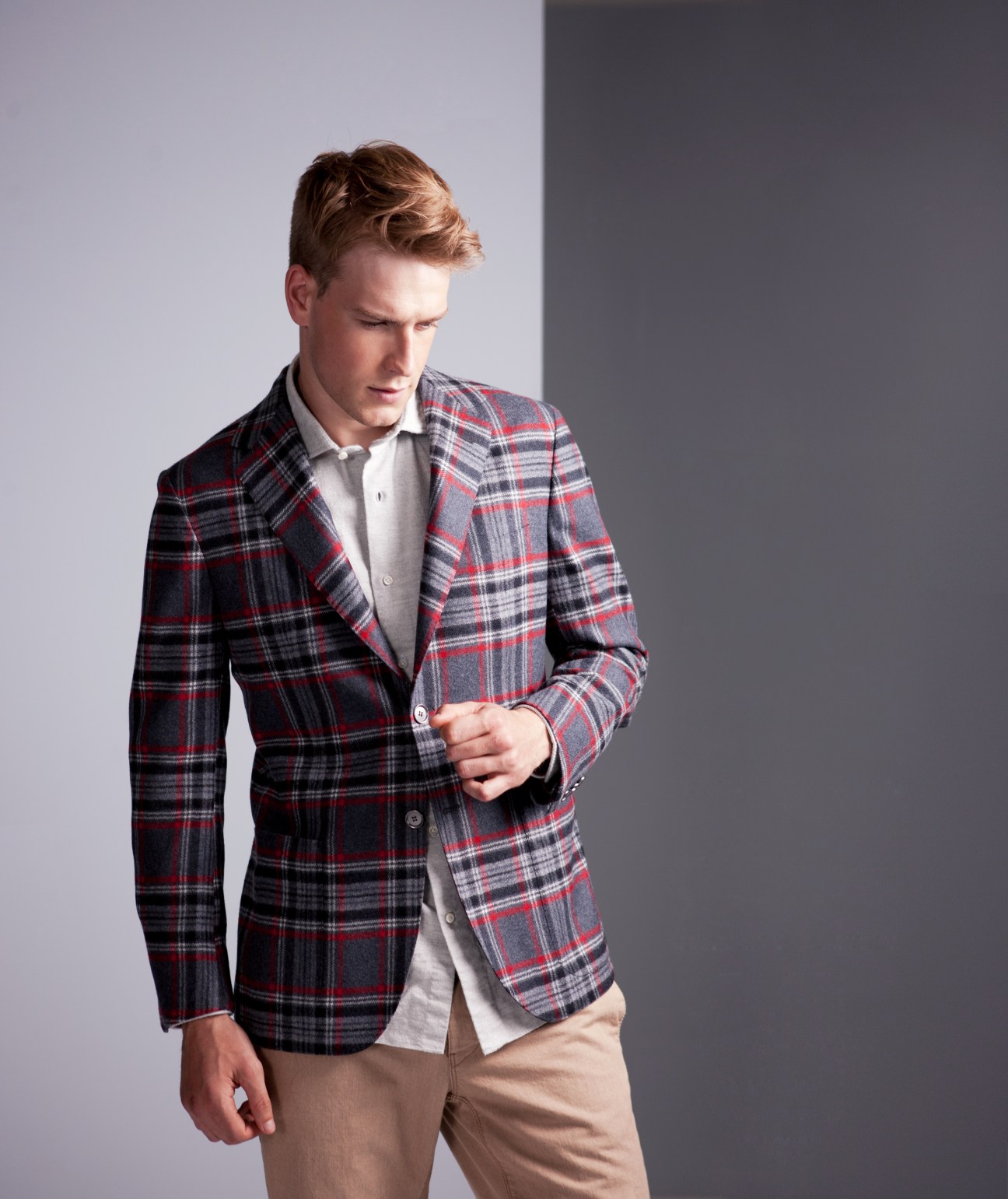 Man wearing red and navy plaid wool jacket with white dress shirt and beige trousers.