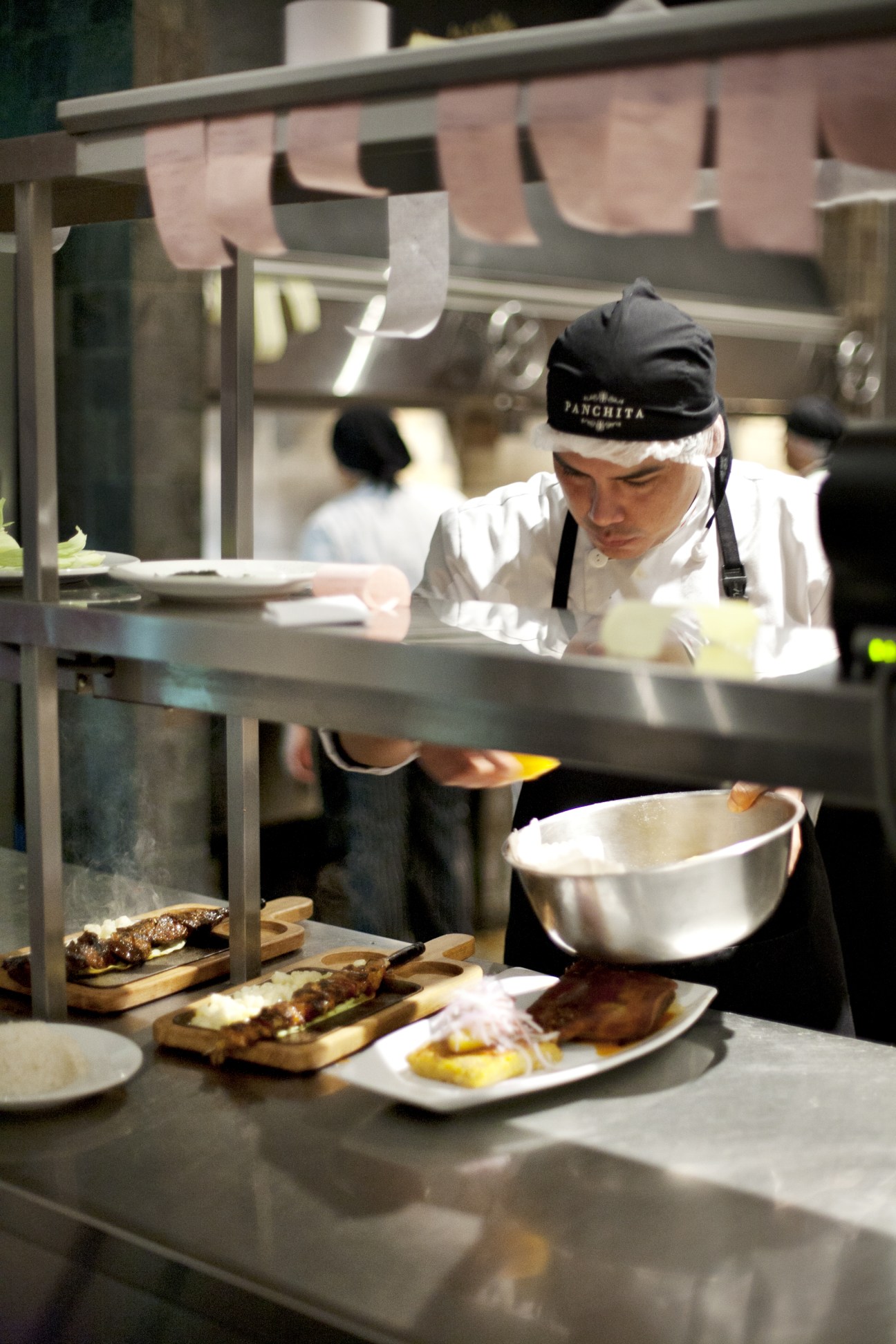 Chef in black Panchita headband prepares Peruvian steak at kitchen counter with plated dishes.