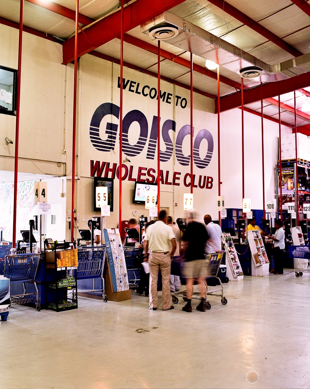 Interior of Goisco wholesale club with red support beams, shoppers with carts, and checkout counters.