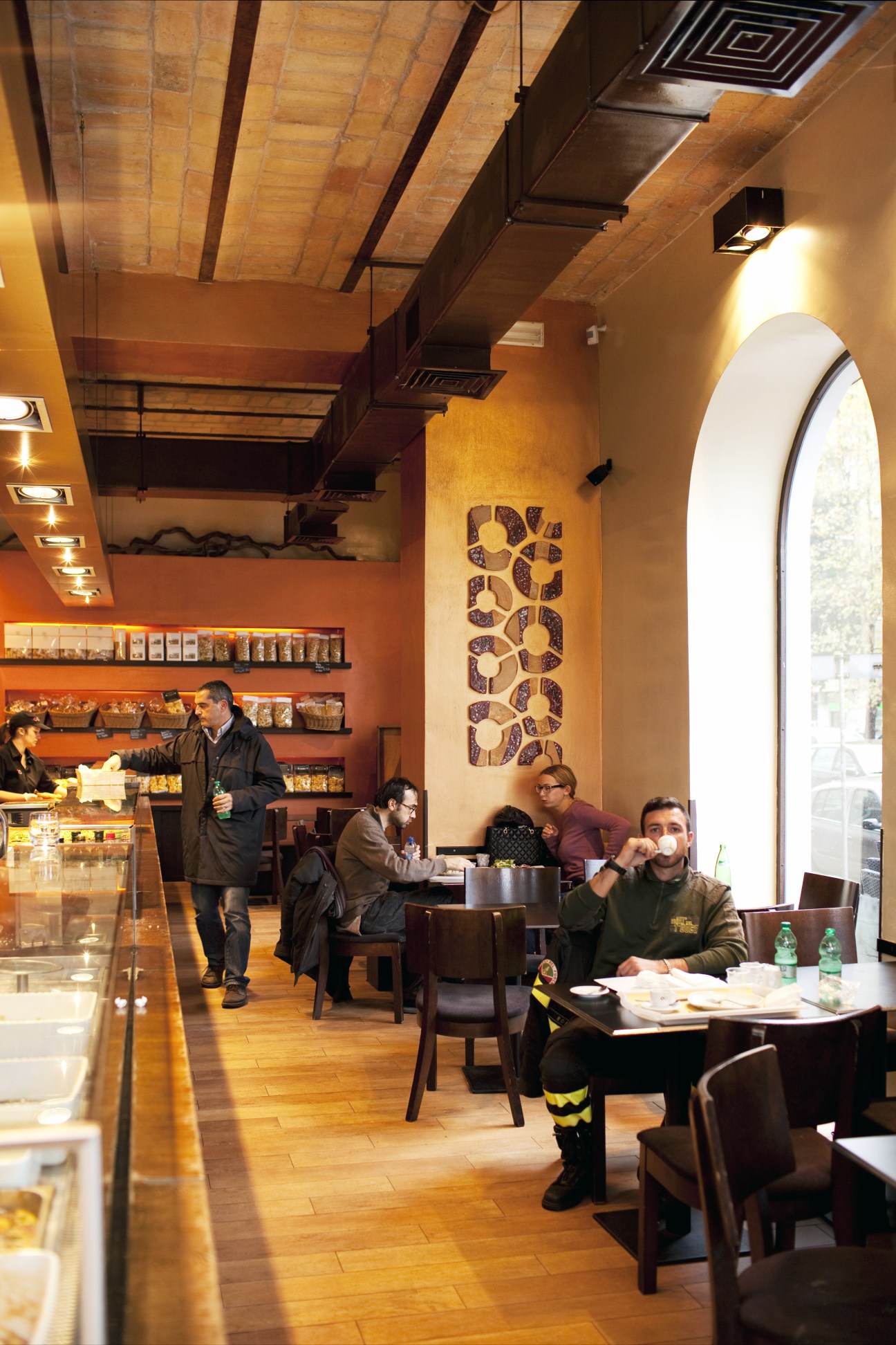 Interior of Doppio Zero bakery/restaurant with wooden ceiling, orange walls, counter, and seated customers.