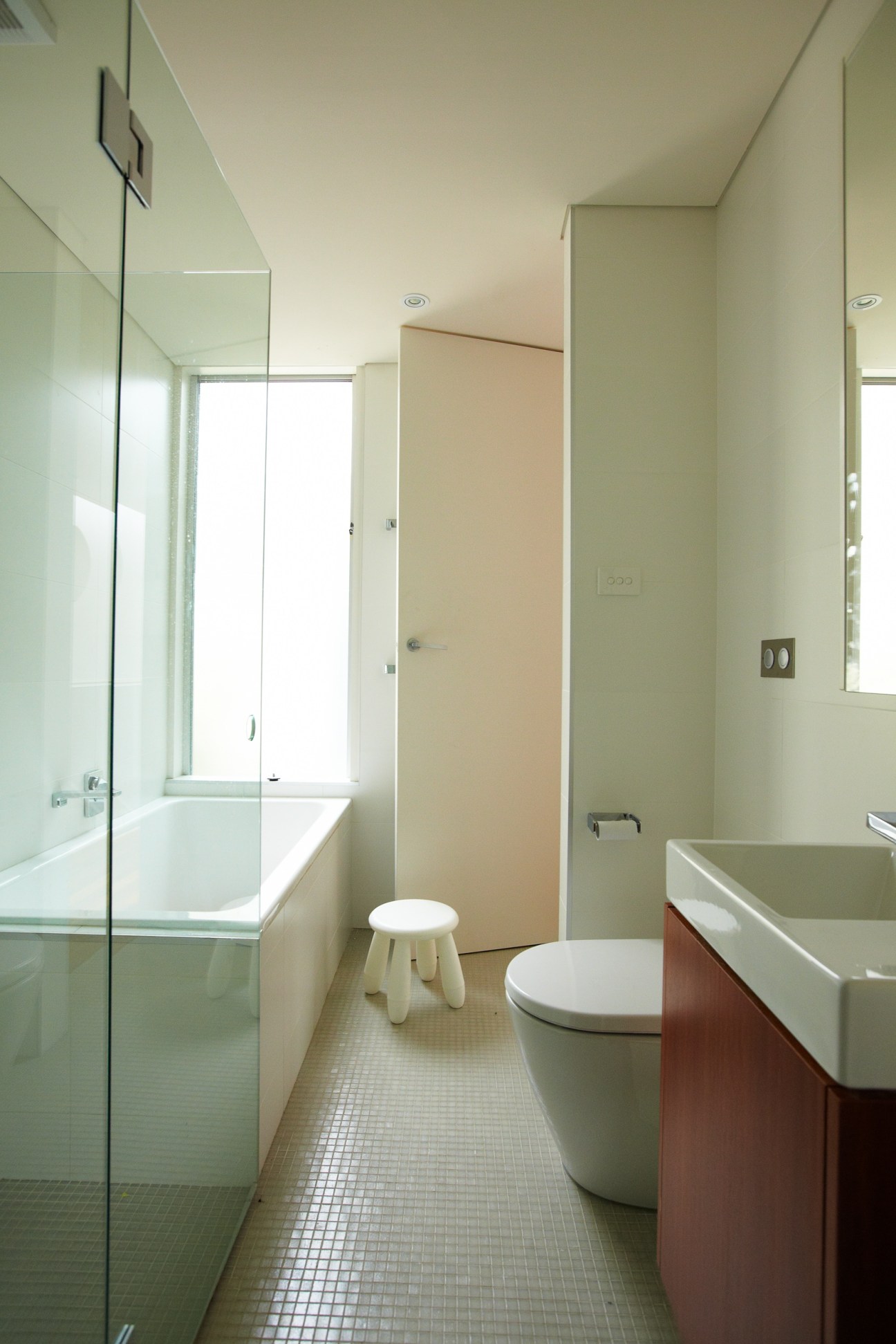 Modern bathroom with white subway tiles, glass shower enclosure, wooden vanity and natural light from window.